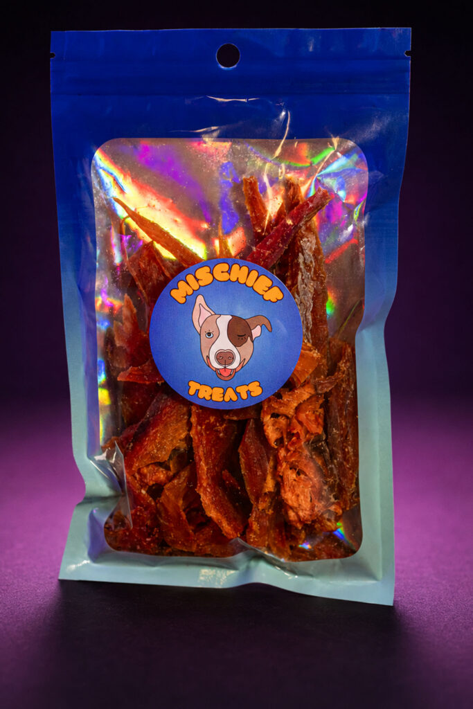 Mischief Treats chicken jerky dog treats in a pouch against a dark studio background